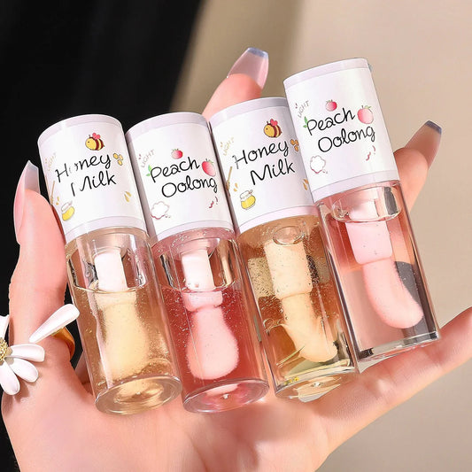 Hand holding four TWG Hydrating Lip Oil Gloss tubes in Honey Milk and Peach Oolong scents with pink and yellow shades, moisturizing and plumping lip glosses